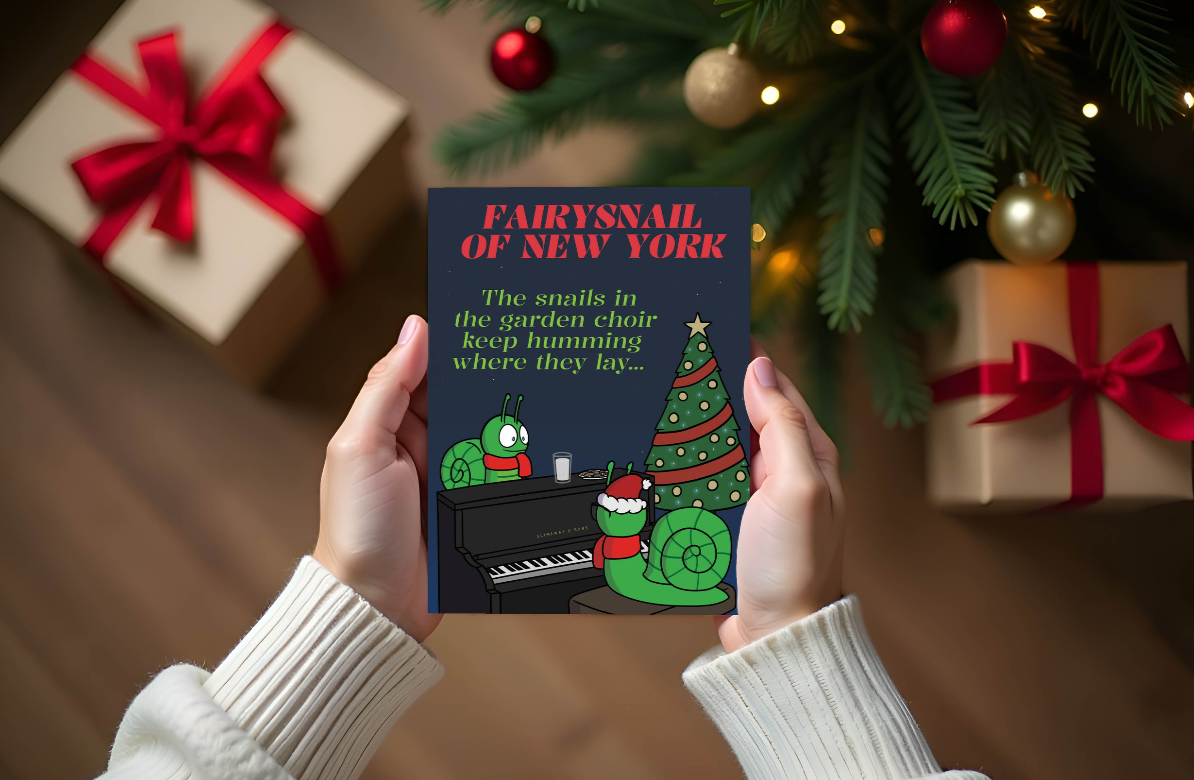 A person holding a Christmas card featuring a cartoon snail with holiday decorations, with a Christmas tree and gifts in the background.