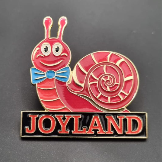 Red snail-shaped pin with a blue bow tie and 'JOYLAND' text on a black background